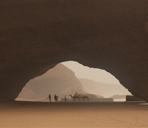 A chap selling camels rides, a metal detectorist and a grand arch at Plage Lgzira